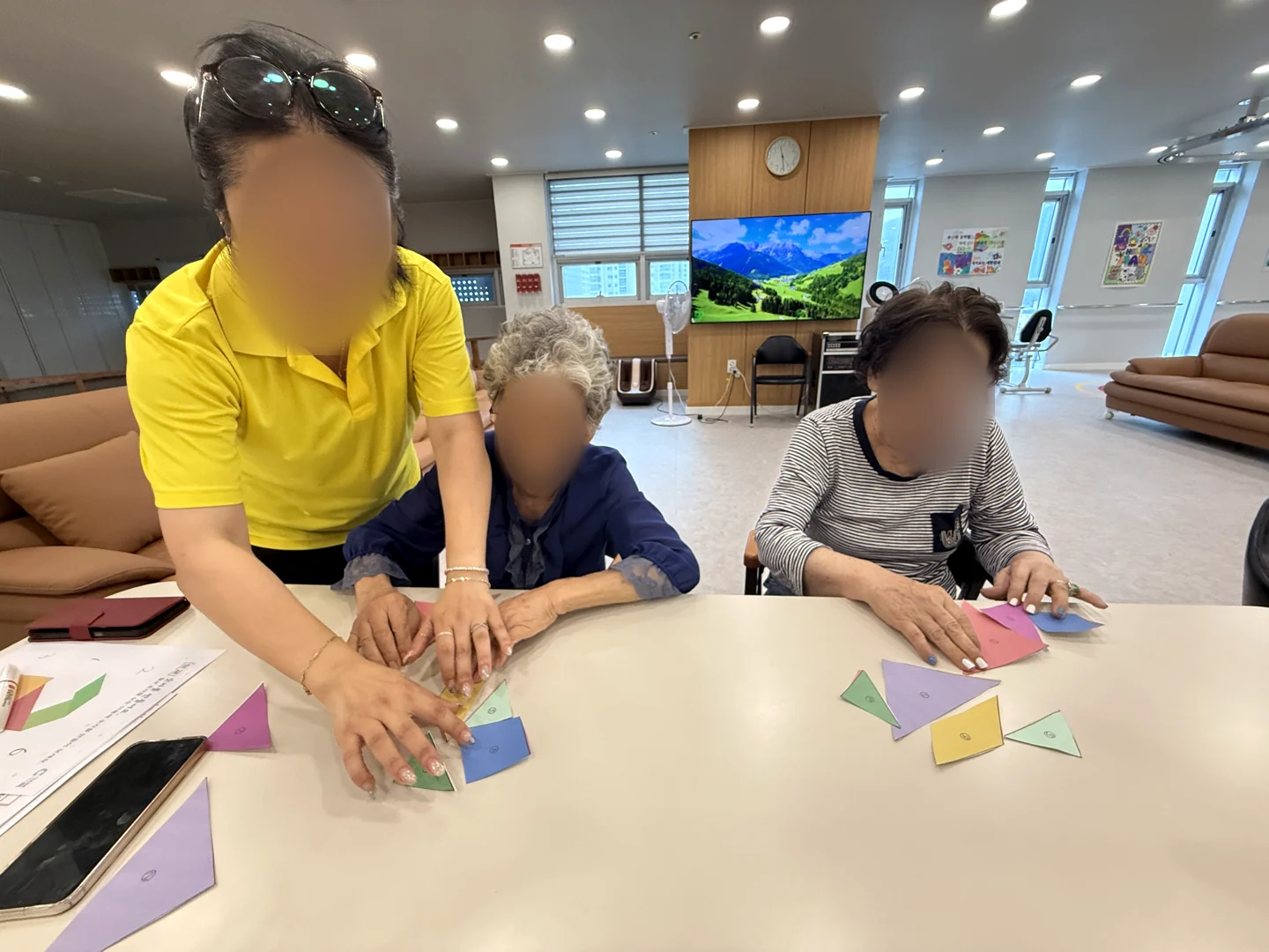 직원이 어르신의 손을 곁에서 도우며 색종이를 접는 모습